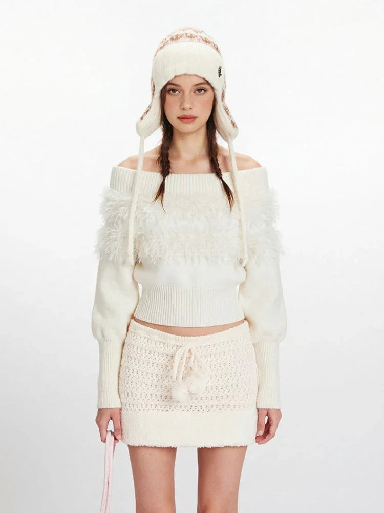 Close-up of a model wearing a white off-the-shoulder sweater with fuzzy trim and a matching mini skirt.