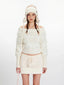 Close-up of a model wearing a white off-the-shoulder sweater with fuzzy trim and a matching mini skirt.