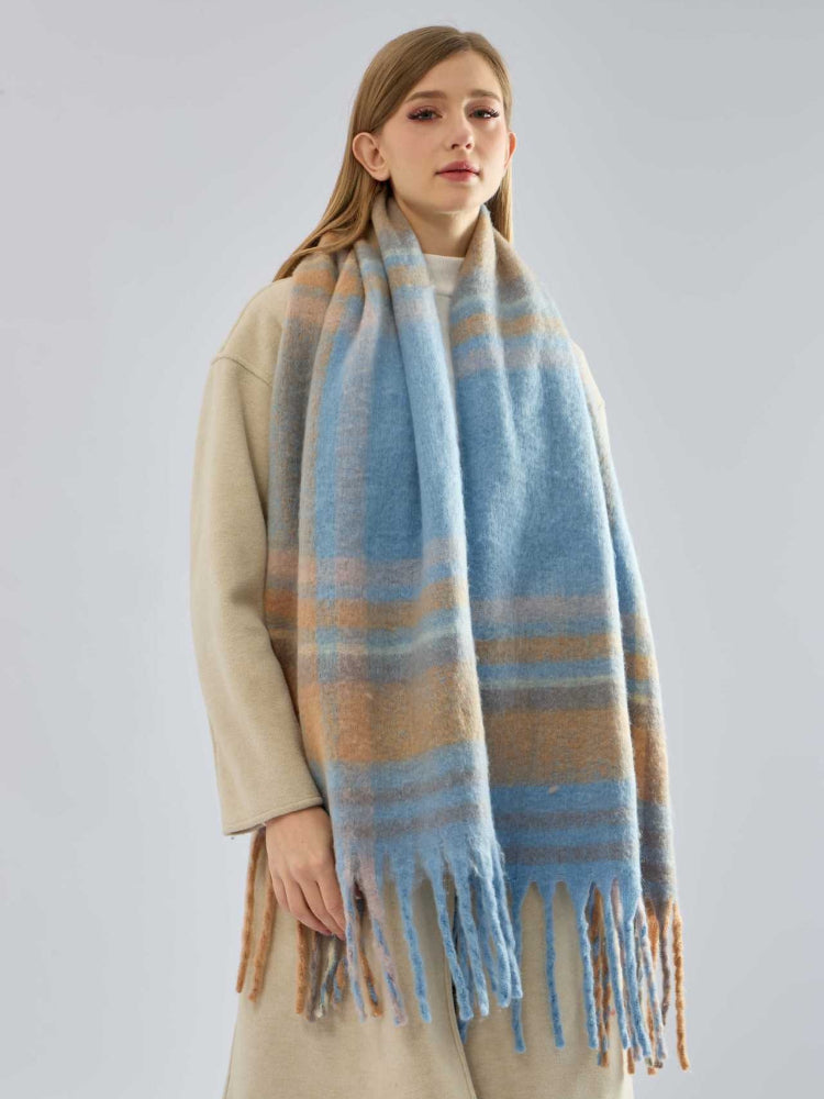 Woman wearing a beige coat and a blue and tan plaid scarf with fringe hanging down.
