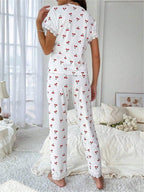 Woman wearing white short-sleeve pajama top with cherry print and white ribbed pants with cherry print, viewed from the back, standing in a bedroom.