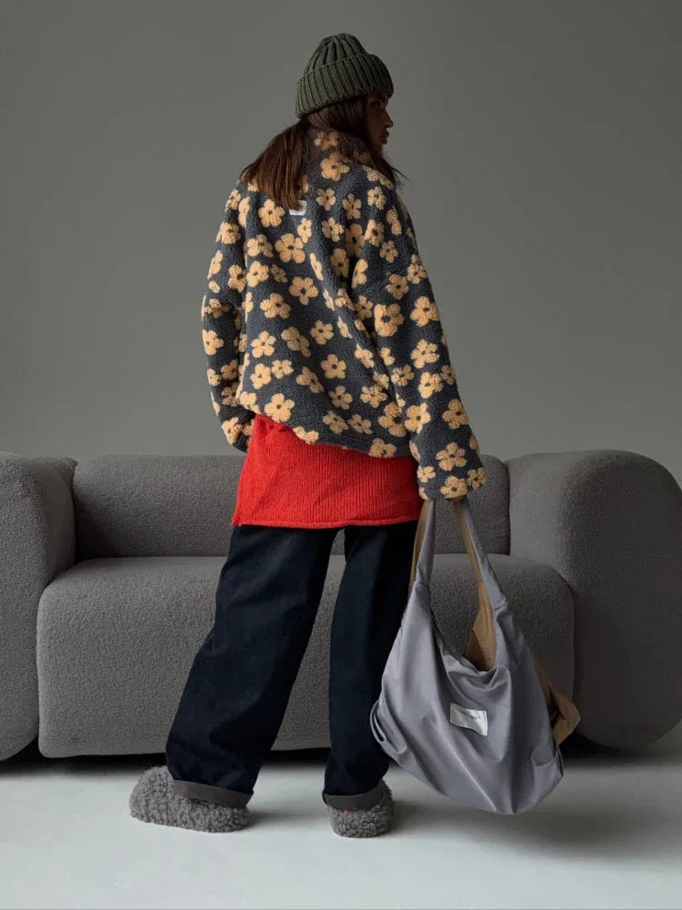 Woman wearing a grey fleece jacket with a yellow floral print, black pants, a red top, and carrying a grey tote bag.