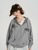 Close-up of a young woman wearing a grey zip-up hoodie with a graphic print, showing the details of the design.
