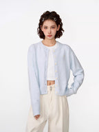 Woman wearing a light blue cropped knit cardigan over a white crop top and cream wide-leg pants.