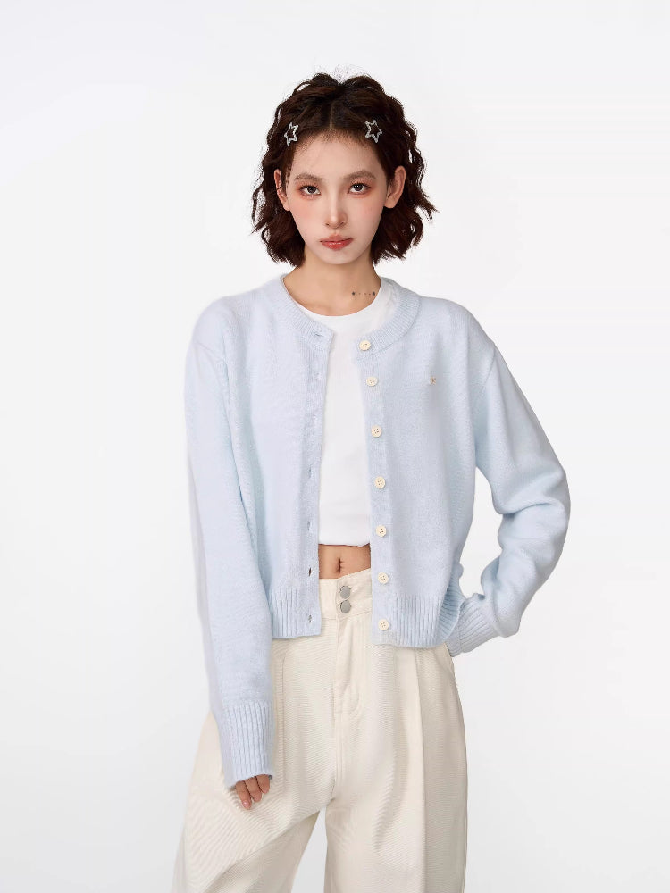 Woman wearing a light blue cropped knit cardigan over a white crop top and cream wide-leg pants.