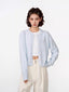 Woman wearing a light blue cropped knit cardigan over a white crop top and cream wide-leg pants.