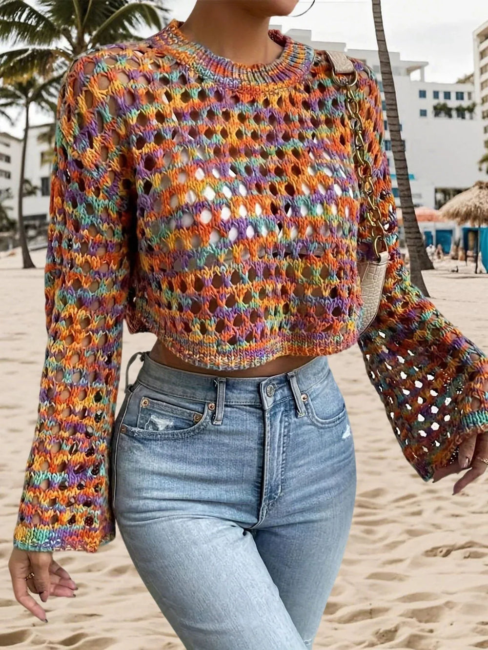 Woman wearing a multicolored open-knit cropped sweater, light-wash denim jeans, and a small crossbody bag.