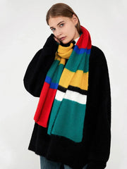 Woman touching her face while wearing a black sweater and a multicolored striped knit scarf