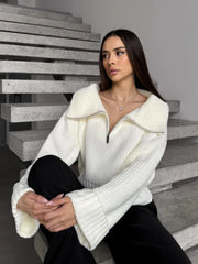 Woman wearing a cream-colored oversized knit sweater with a half-zip neckline and wide sleeves, sitting on stairs.