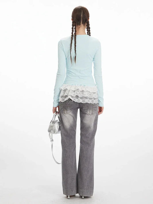 Back view of a woman wearing a light blue long-sleeve top with white lace trim and grey wide-leg jeans with embellishments.