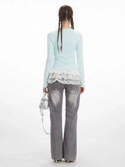 Back view of a woman wearing a light blue long-sleeve top with white lace trim and grey wide-leg jeans with embellishments.