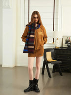 Woman in a brown bomber jacket, mini skirt, and black boots, wearing a striped scarf.