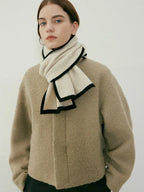 Woman wearing a beige textured coat and a cream scarf with black trim