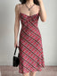 Full body shot of a woman in a red plaid midi dress, styled with a black necklace and handbag.