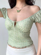 Model wearing a light green floral print top with puff sleeves and a sweetheart neckline, styled off-the-shoulder.