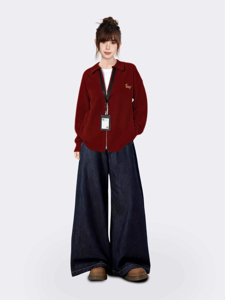 Woman modeling a maroon zip-up knit cardigan with a collared neckline and long sleeves, paired with dark wash wide-leg jeans and brown shoes.
