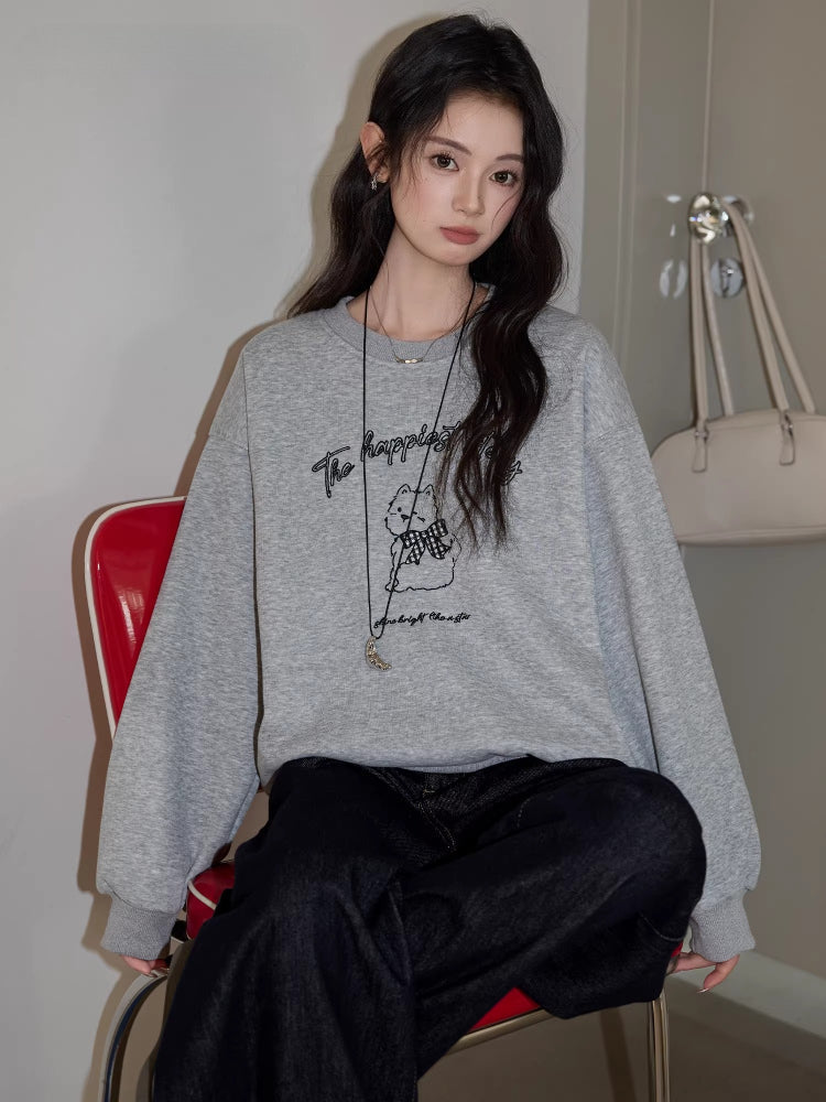 Woman sitting on a red chair wearing a grey crew neck sweatshirt with a graphic print