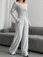 Model wearing a grey ribbed knit long sleeve top and wide leg pants set, standing indoors.