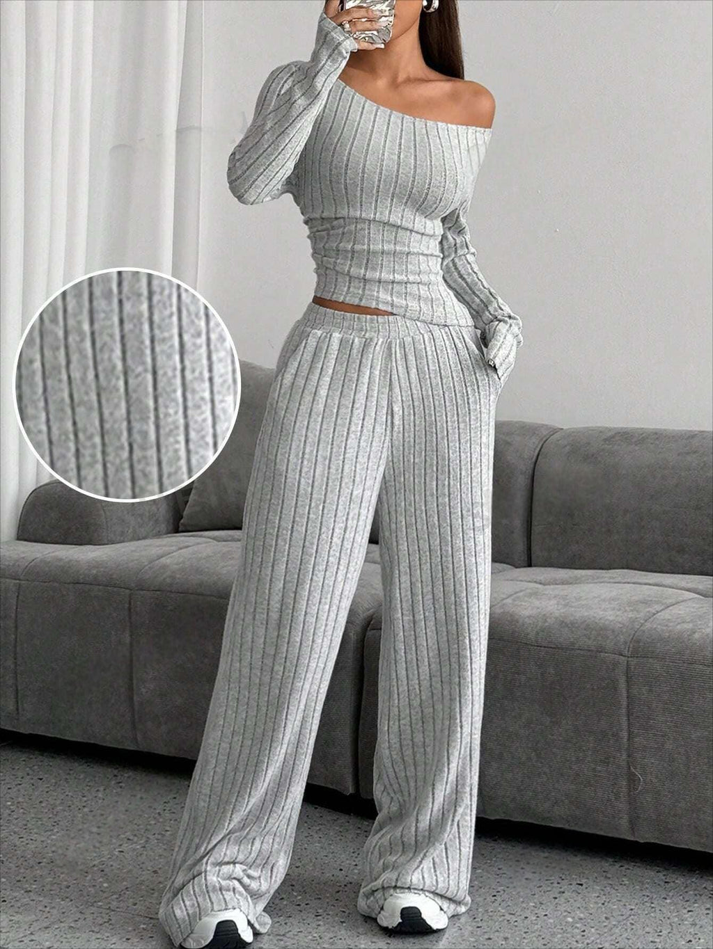 Close-up of the ribbed texture of the grey knit set worn by the model, standing indoors.
