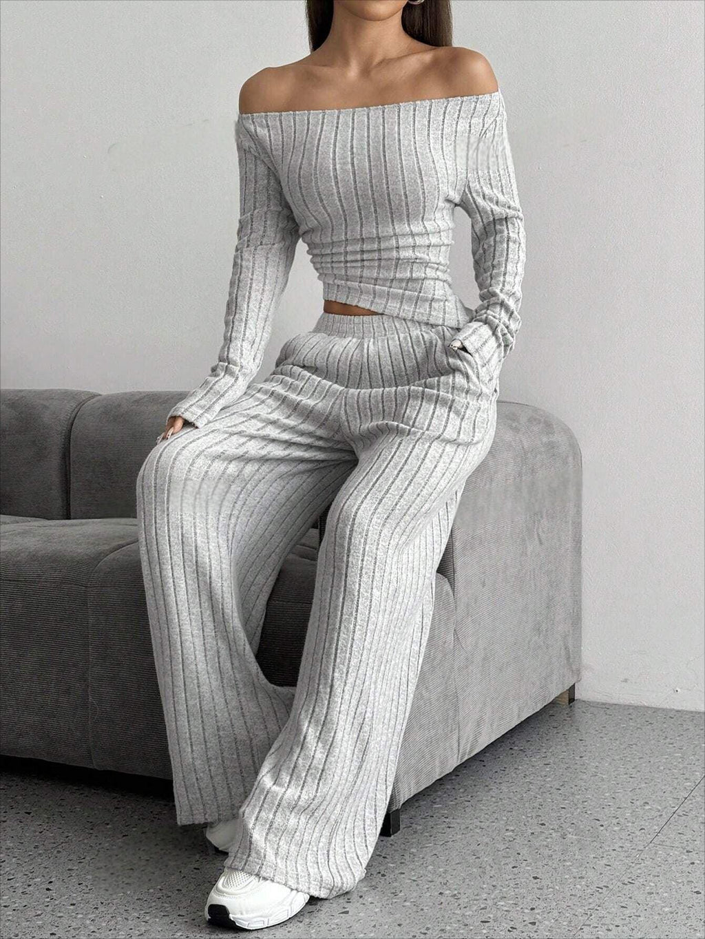Model sitting on a sofa wearing a grey ribbed knit off-the-shoulder long sleeve top and wide leg pants set.