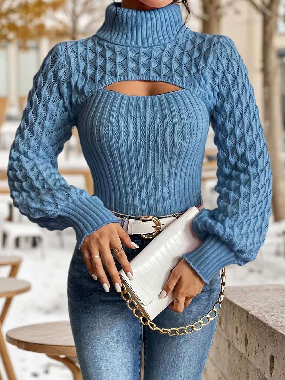 Front view of a woman wearing a blue knit turtleneck top with a cut-out detail and balloon sleeves, accessorized with a white belt and clutch.