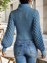 Back view of a woman wearing a blue knit turtleneck top with a cut-out detail and balloon sleeves.