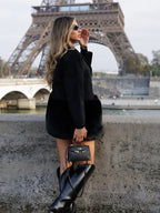 Woman wearing a black wool blend coat with faux fur accents, black top, and black boots, with the Eiffel Tower in the background.
