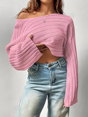 Woman wearing a pink cropped knit sweater off the shoulder, revealing her midriff and a belly piercing.