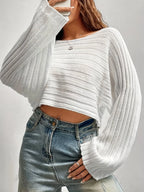 Woman adjusting the front of a white cropped knit sweater, showing a hint of her midriff.