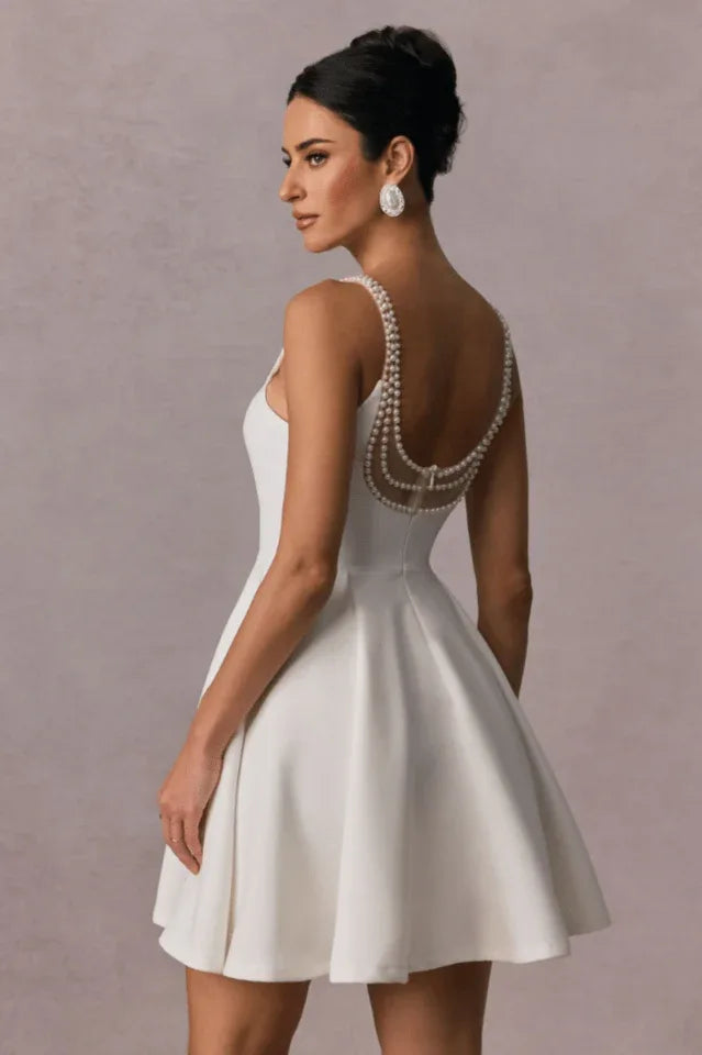 Back view of a woman in a short white A-line dress with pearl detailing on the straps and back