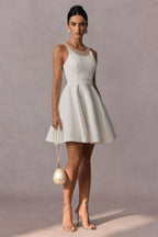Woman holding a pearl handbag and wearing a short white A-line dress with pearl embellishments