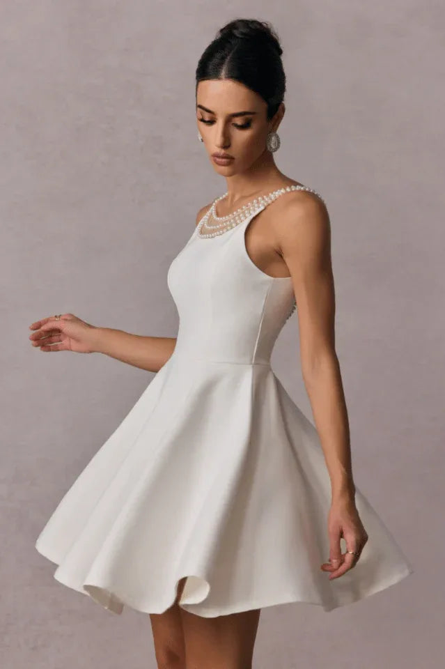 Side view of a woman in a short white A-line dress with a pearl neckline