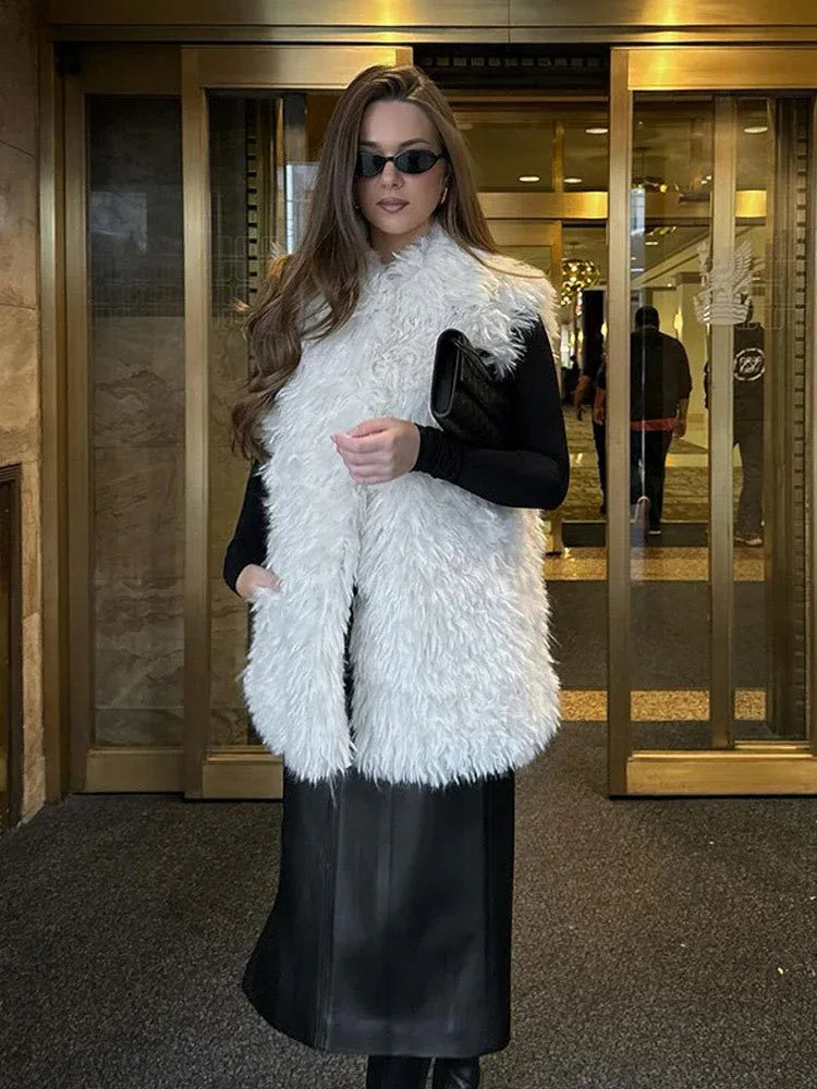 Woman wearing a white shaggy faux fur vest over a black long-sleeve top and black skirt, holding a black clutch. Main image