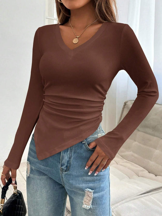 Close-up of a woman's torso wearing a brown long-sleeved ribbed knit top with a v-neck and asymmetrical hem.