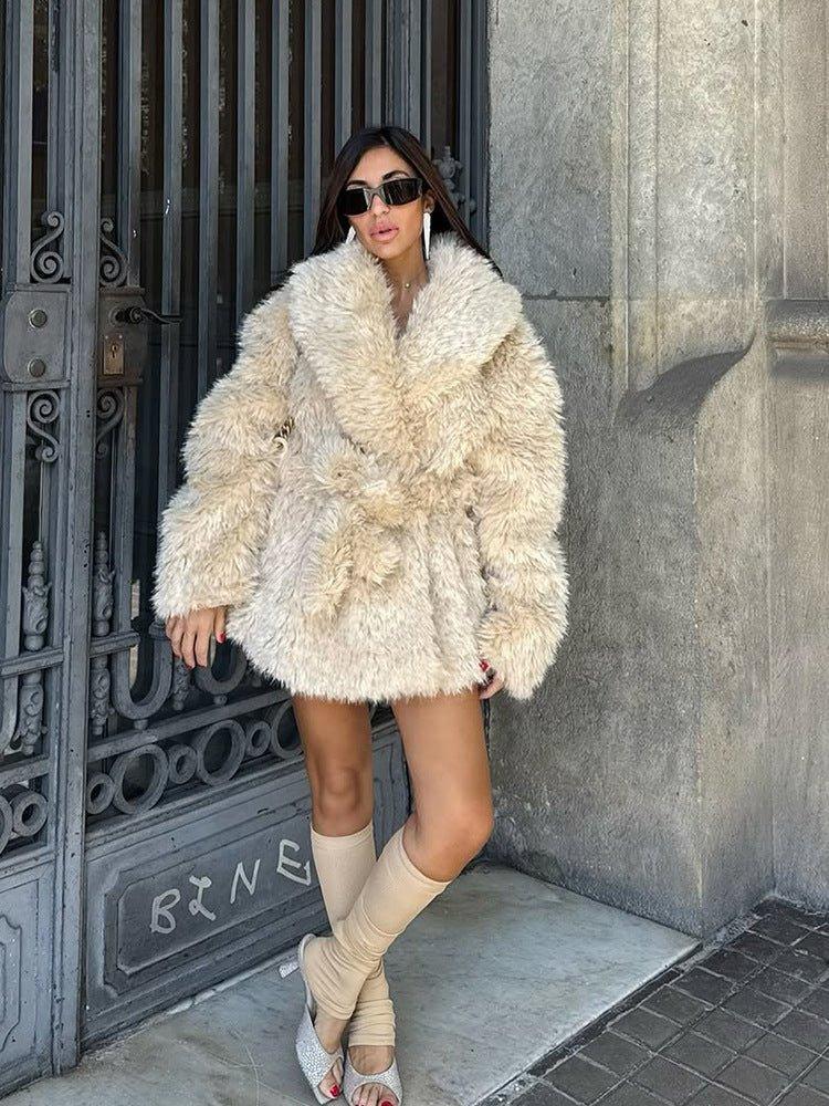 woman wearing a cream faux fur coat with a large collar and a belt, standing with legs apart