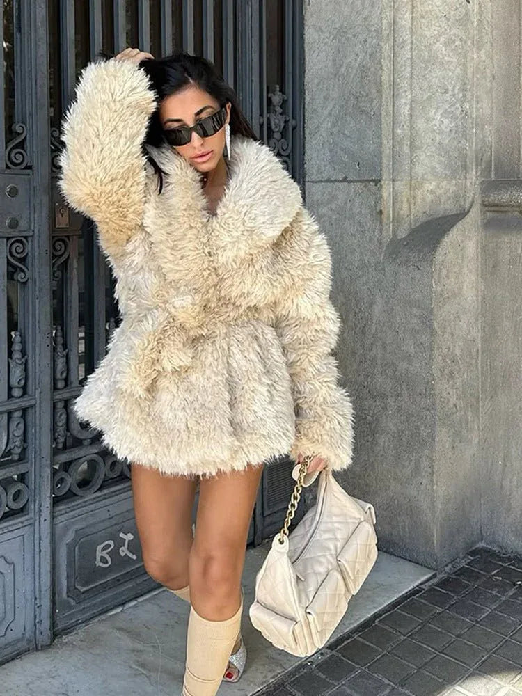 woman in a cream faux fur coat with a large collar and a belt, touching her hair