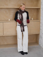 Model wearing a cream and black sweater with an argyle scarf and white pants
