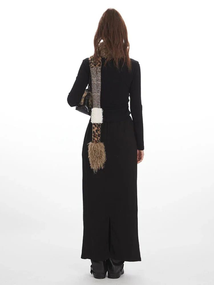Back view of a model wearing a black long-sleeve top and a black maxi skirt with a drawstring waist and white star graphics, accessorized with a multi-patterned scarf.