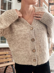 Woman wearing a beige chunky knit cardigan with a V-neck and wooden buttons.
