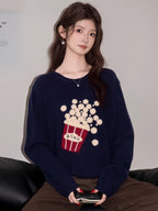 Woman wearing a navy blue knit sweater with a popcorn graphic and Korean text, paired with brown pants.