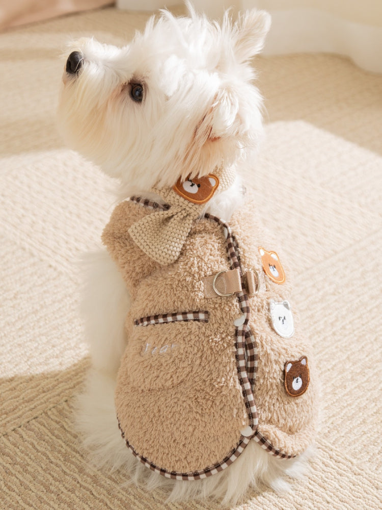 Side view of a white dog wearing a tan fleece vest with embroidered bear appliques and a checkered trim.