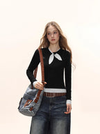Close-up of a model wearing a black long-sleeve top with a white polka dot scarf detail and white polka dot cuffs, carrying a denim crossbody bag.