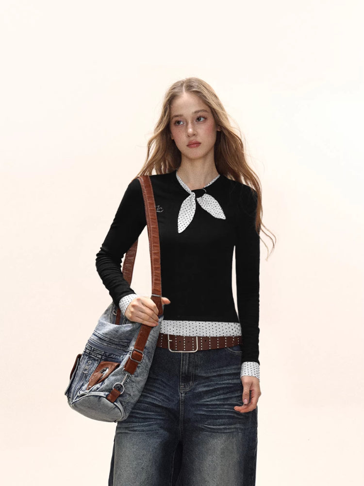 Close-up of a model wearing a black long-sleeve top with a white polka dot scarf detail and white polka dot cuffs, carrying a denim crossbody bag.