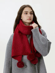 Woman adjusting a red knit scarf with pom-pom embellishments