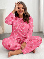 Woman wearing pink heart-print pajamas, sitting cross-legged and making an 'okay' gesture.