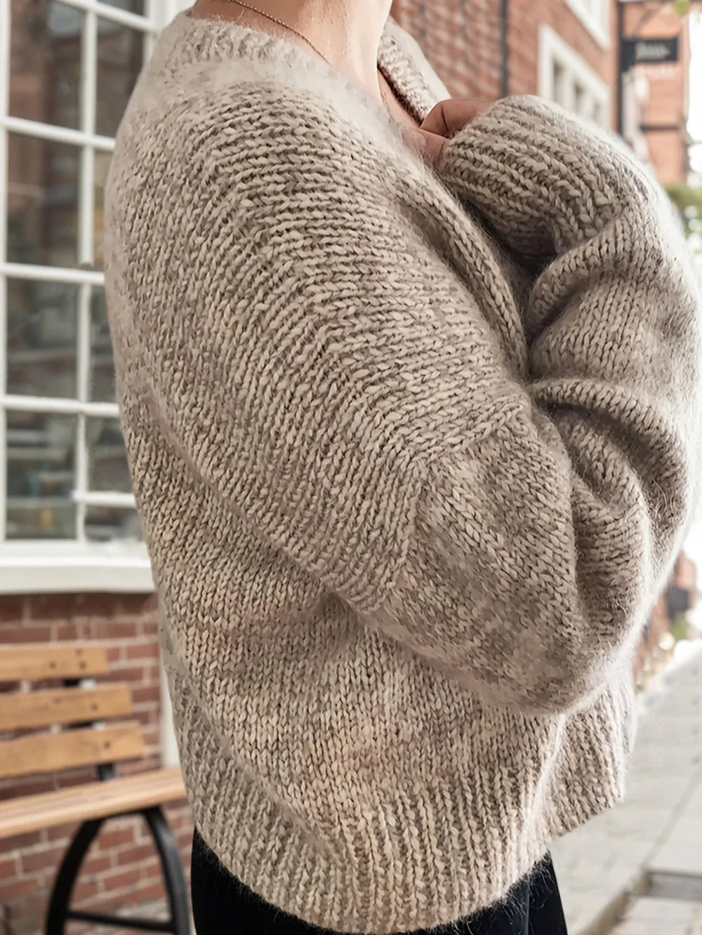 Side view of a woman wearing a beige knit cardigan with her arms crossed.