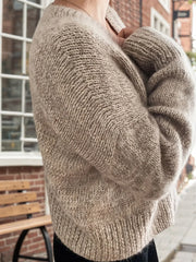 Side view of a woman wearing a beige knit cardigan with her arms crossed.
