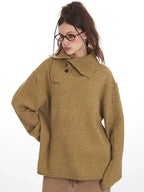 Close-up of a model wearing a tan oversized knit sweater with a wide collar and button detail, hands on hips.
