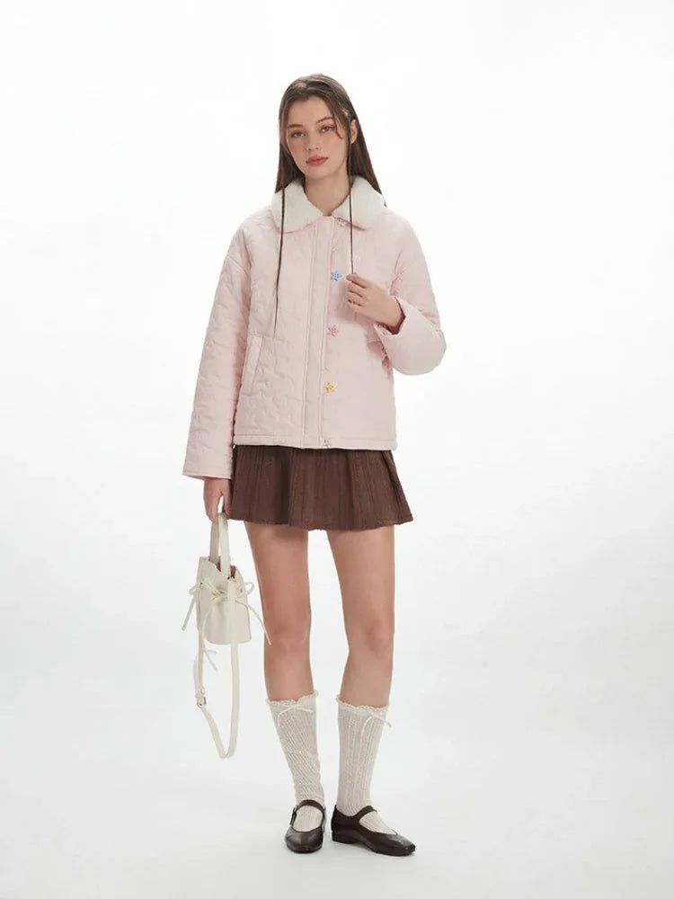 Model in a pink quilted jacket, brown skirt, and white socks, with a white bucket bag.