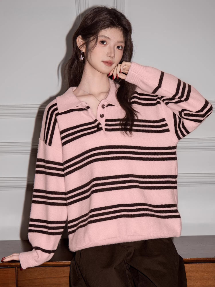 Woman wearing a pink and black striped knit polo sweater and brown pants, posing with her hand on her cheek.