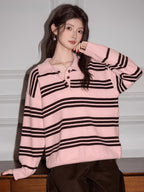 Woman wearing a pink and black striped knit polo sweater and brown pants, posing with her hand on her cheek.